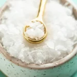 Gold spoon scooping flaky sea salt from a bowl